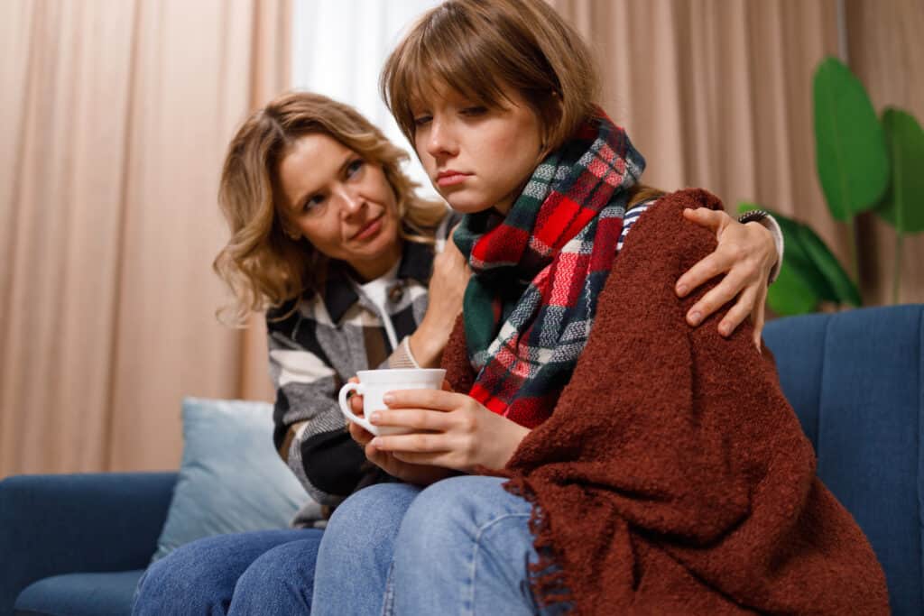 caring mother supporting her sad daughter during flu illness