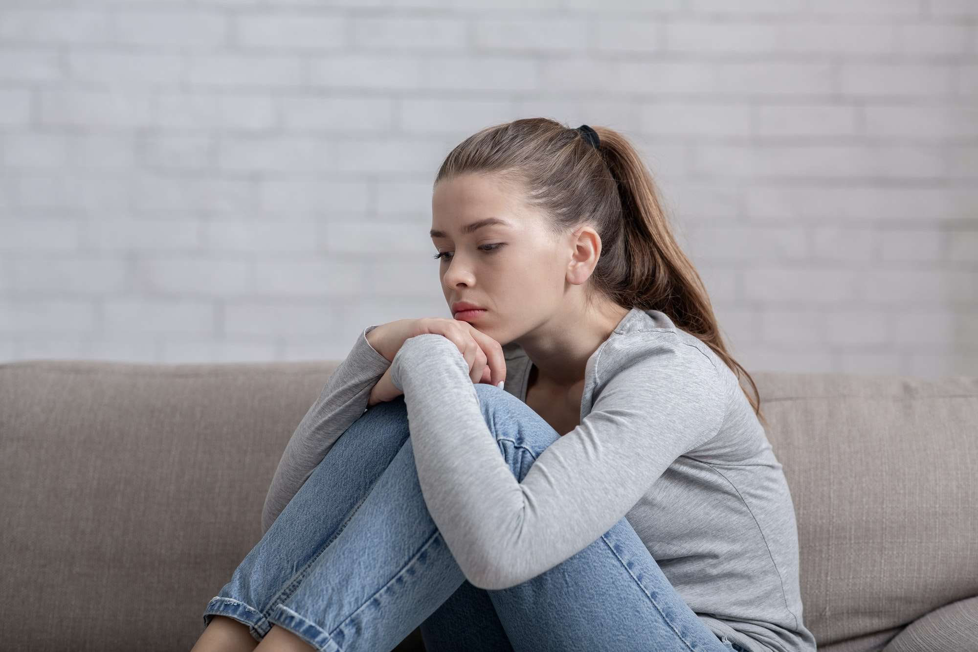 Young woman with depression sitting alone on sofa at home